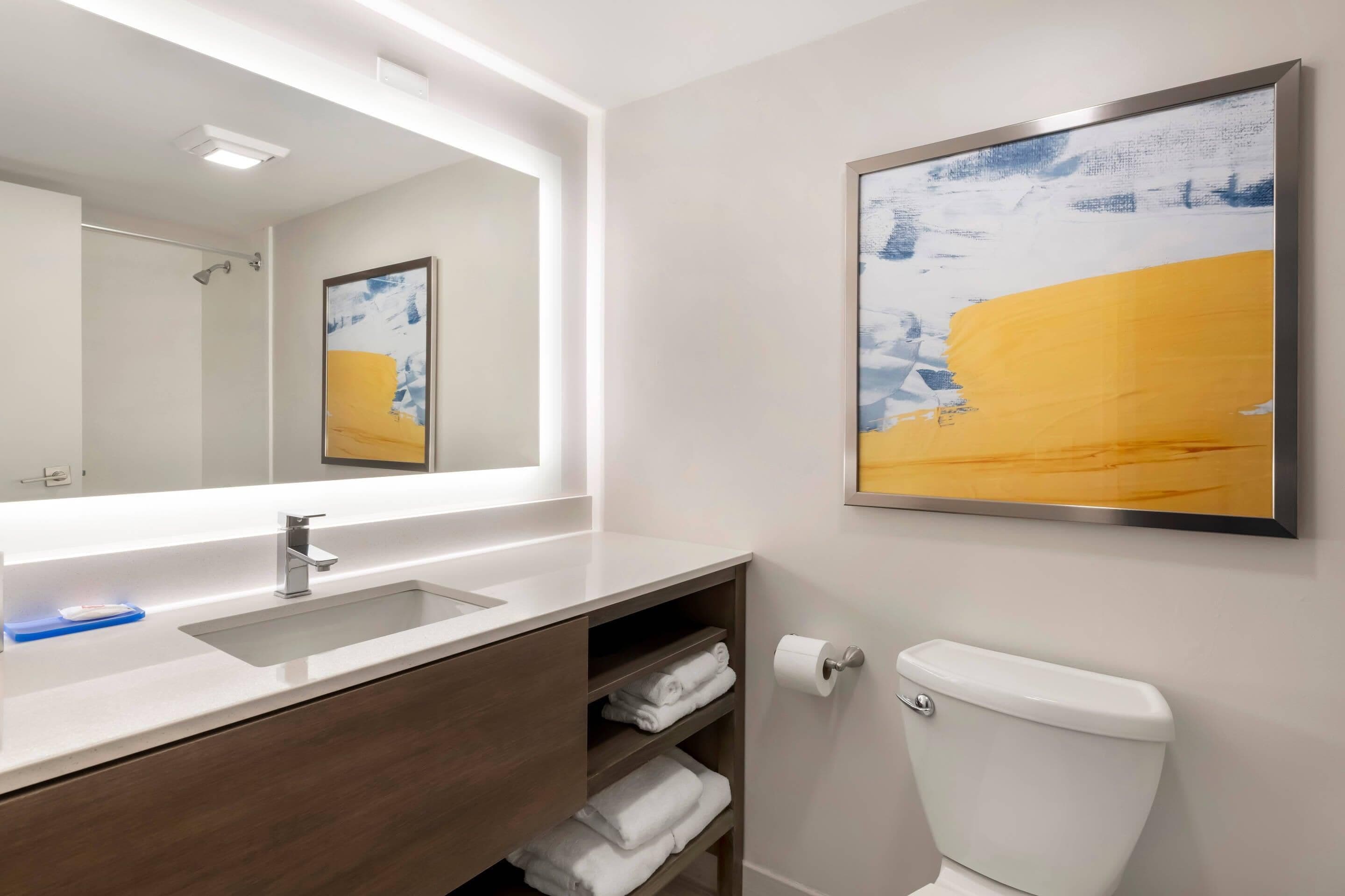 A bathroom with a white sink, a mirror, a toilet, and a shelf with towels.