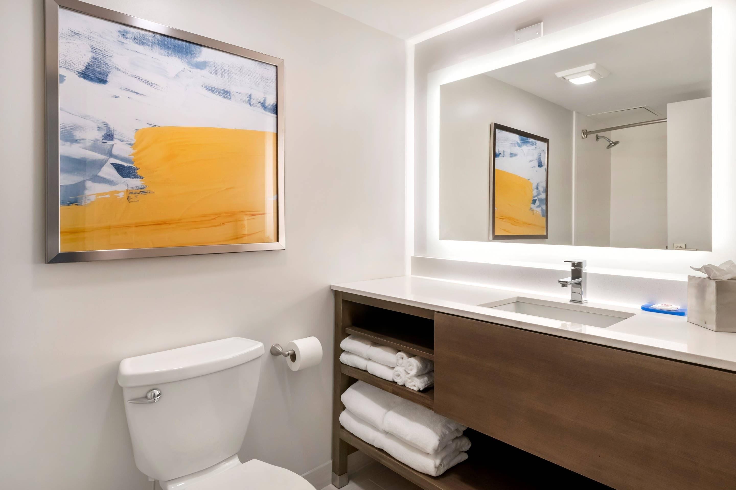 Un baño moderno con inodoro, lavabo, espejo y estante con toallas.