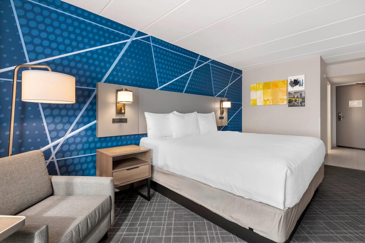 A modern hotel room with a large bed, a sofa, a nightstand, and a wall with geometric patterns.