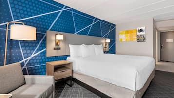 Une chambre d’hôtel moderne avec un grand lit, un canapé, une table de chevet et un mur orné de motifs géométriques.