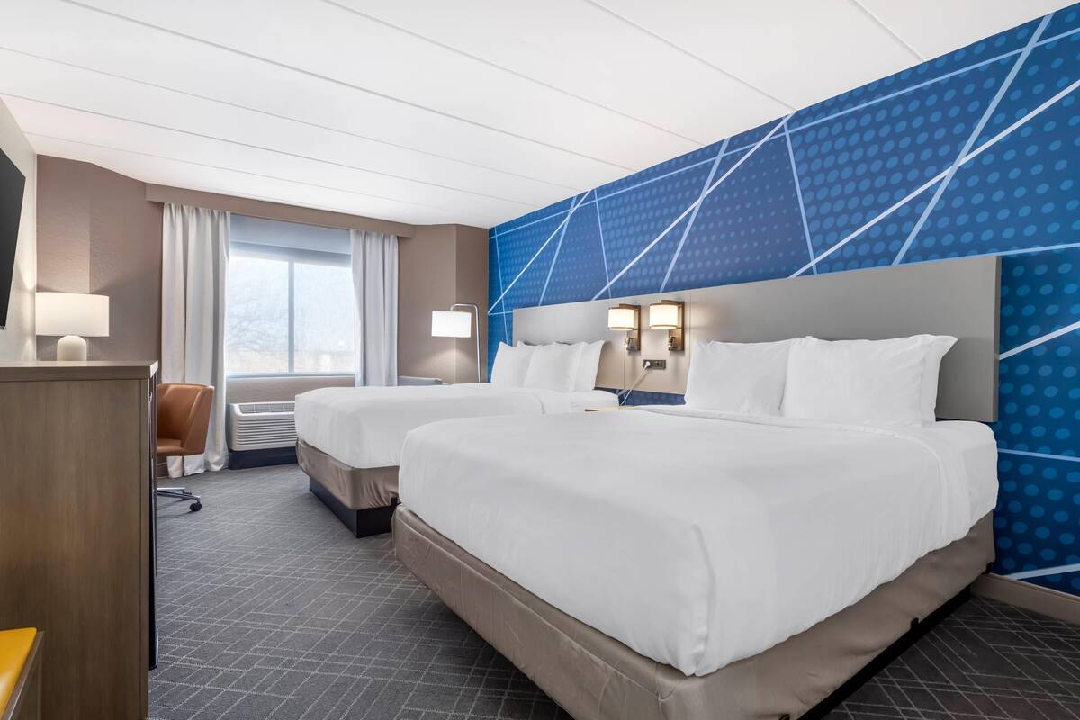 A hotel room with two beds, a desk, a chair, and a large window.