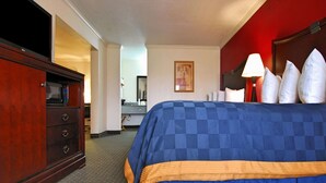 A hotel room with a large bed, a wooden dresser, a desk, and a bathroom visible in the background. - Americas Best Value Inn Kingsville (Kingsville)