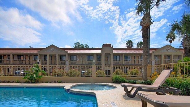 A swimming pool with lounge chairs, a hot tub, and a hotel building with balconies in the background. - Americas Best Value Inn Kingsville (Kingsville)