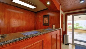 A reception desk with a wooden finish, a framed artwork on the wall, and a view of the outside through a glass door. - Americas Best Value Inn Kingsville (Kingsville)