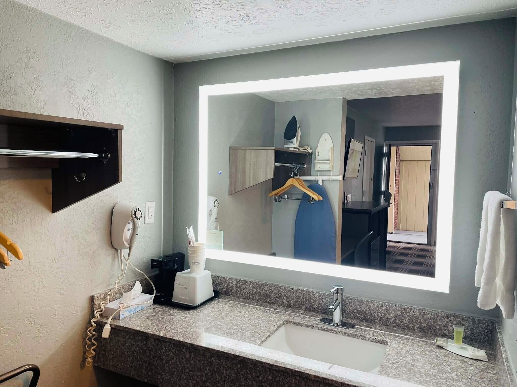A bathroom with a large mirror, a sink, a towel rack, and a coffee maker.
