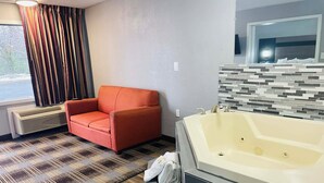 A modern bathroom with a large bathtub, a red armchair, and a patterned floor.