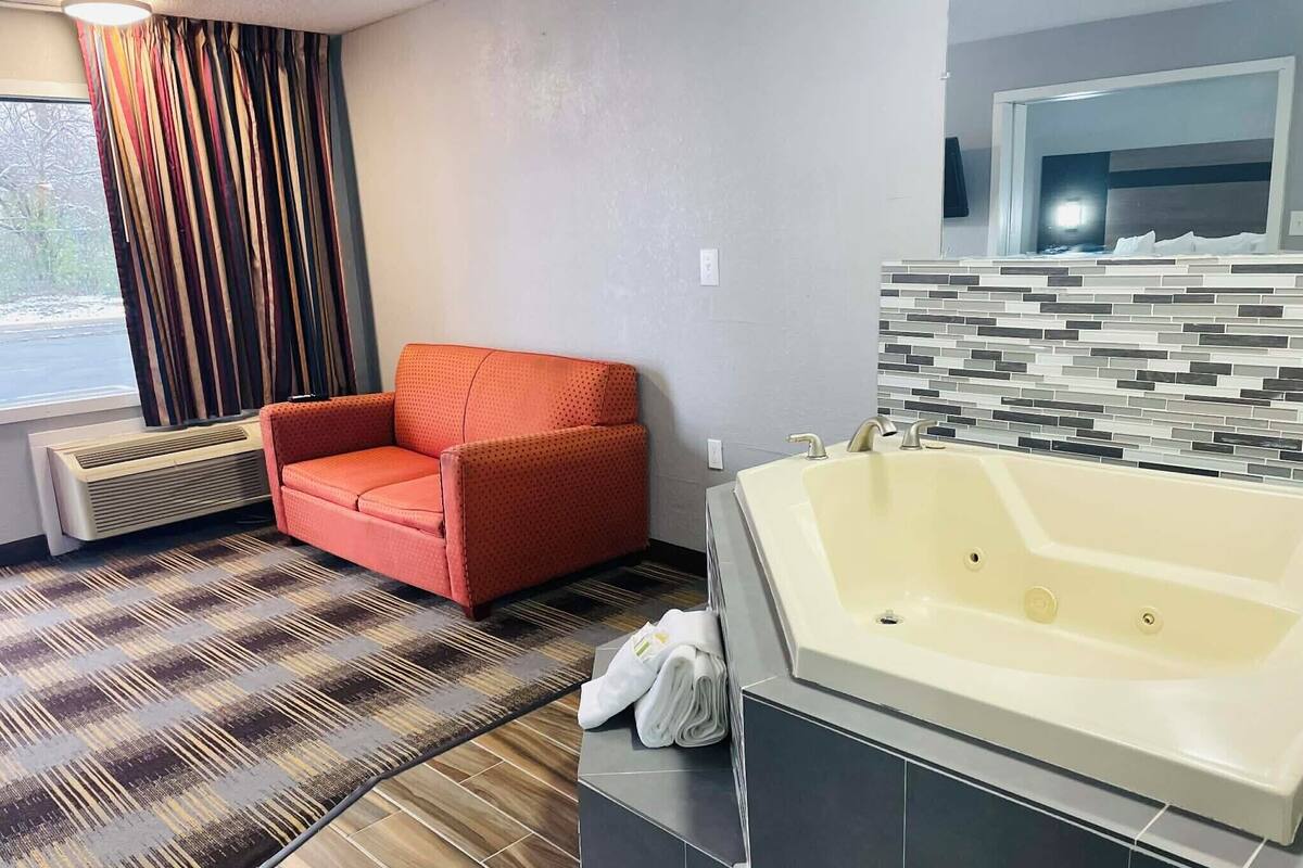 Un baño moderno con una bañera grande, un sillón rojo y un suelo con estampado.