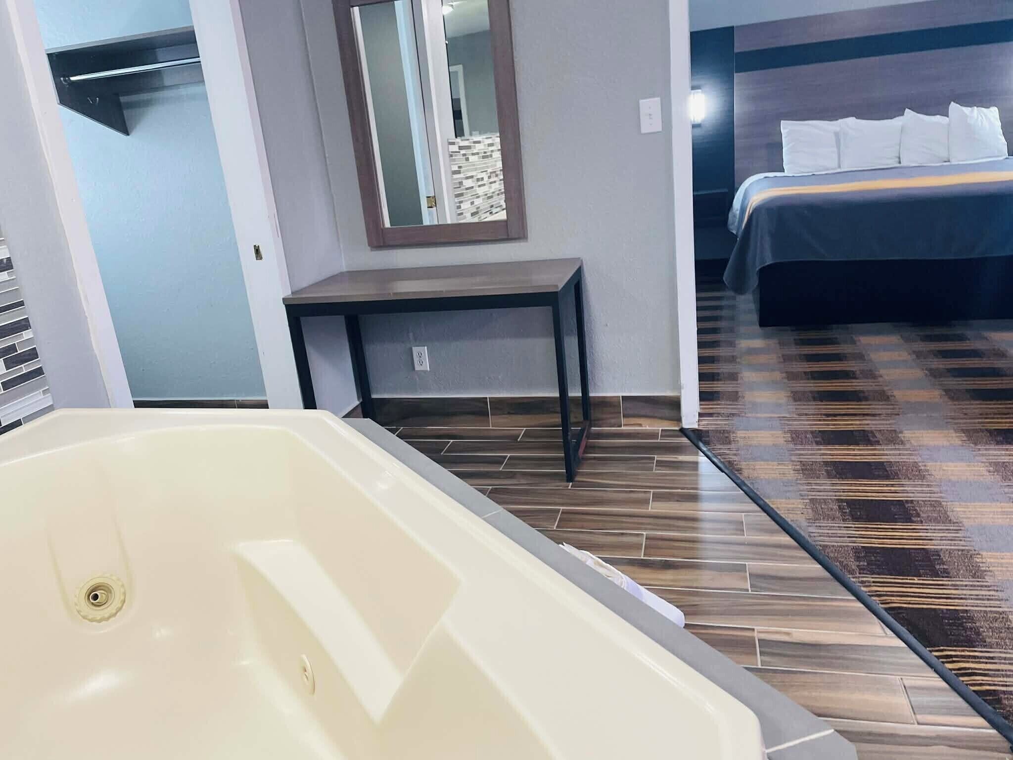 Une chambre d ’hôtel avec une grande baignoire, une petite table, un lit avec du linge de lit blanc et un miroir au mur.
