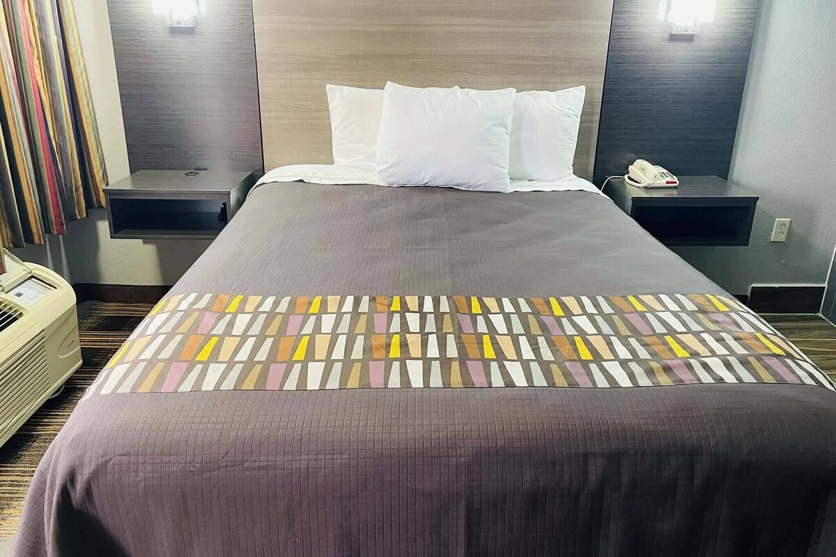 Una habitación de hotel con una cama grande, dos mesitas de noche, un teléfono y una lámpara fijada a la pared.