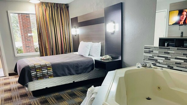 A modern hotel room with a large bed, a separate bathroom with a bathtub, a flat-screen TV, and a window with curtains.