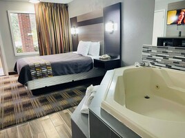 Una habitación de hotel moderna con una cama grande, un baño independiente con bañera, un televisor de pantalla plana y una ventana con cortinas.