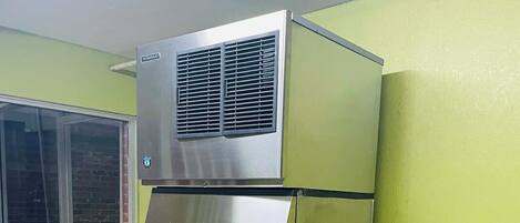 A commercial ice dispenser with a digital control panel, located in a room with green walls and a window.