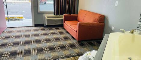 Hotellihuone, jossa on suuri ikkuna, punainen sohva, kuviollinen matto, puulattia ja kylpyamme.