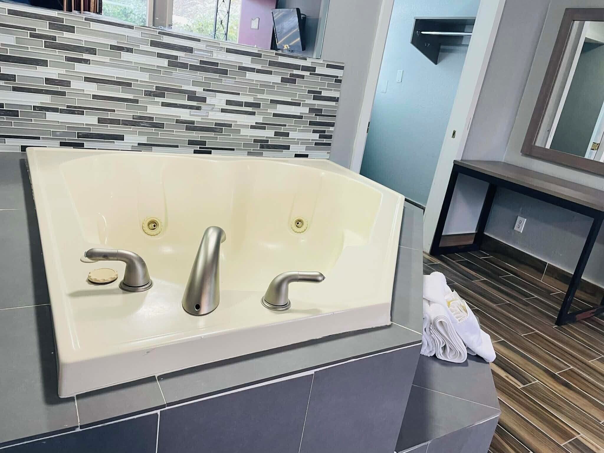 Un baño moderno con una bañera grande, un rebozo de azulejos y piso de madera.