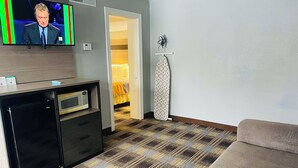 A hotel room with a flat-screen TV, a minibar, a microwave, a patterned carpet, and a sofa.