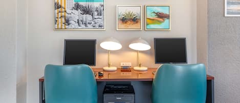 A workspace with two blue chairs, a desk, two speakers, and three framed artworks on the wall.