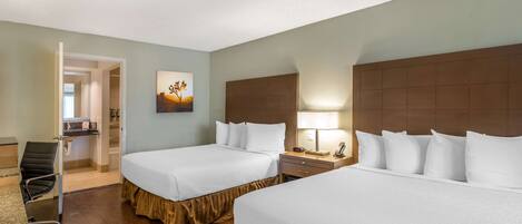 A hotel room with two beds, a desk, a chair, a nightstand with a lamp, and a painting on the wall.