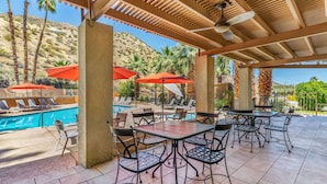 An outdoor pool area with lounge chairs and umbrellas, a covered patio with tables and chairs, and a mountainous backdrop. - Best Western Inn at Palm Springs (Palm Springs)