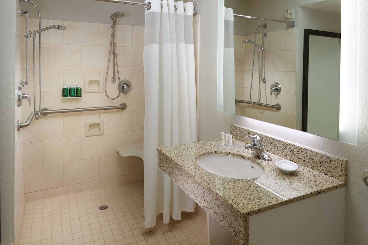 A bathroom with a sink, mirror, shower, and grab bars.