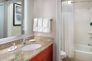 A bathroom with a granite countertop sink, a mirror, a towel rack with white towels, a shower curtain, and a toilet.