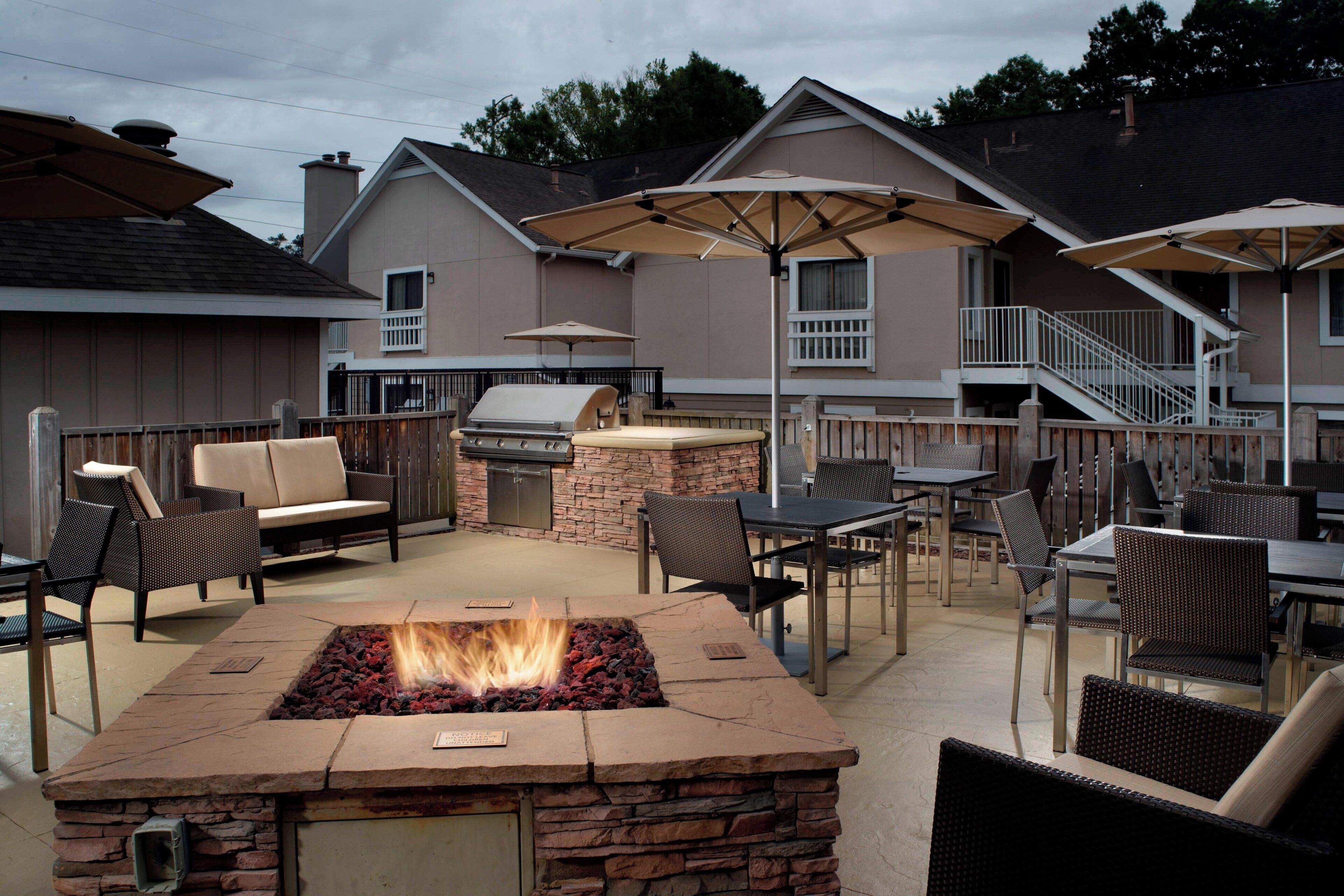 An outdoor patio with a stone fire pit, seating, and a grill.