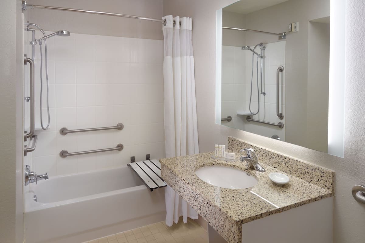 A bathroom with a bathtub, a sink, a mirror, and grab bars.