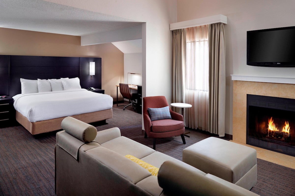 A hotel room with a bed, a sofa, a chair, a TV, and a fireplace.