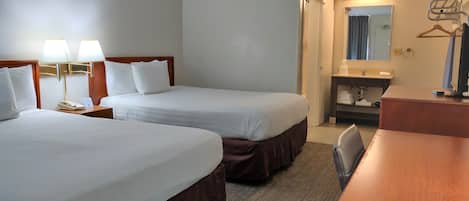 A hotel room with two single beds, a desk, a chair, a bathroom with a mirror, and a coat rack.