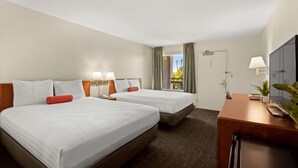 Ett hotellrum med två sängar, ett skrivbord, en tv och ett fönster med gardiner.