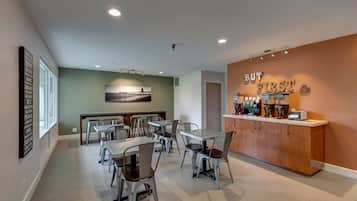 A modern dining area with tables and chairs, a kitchen counter with appliances, and a wall with motivational text.