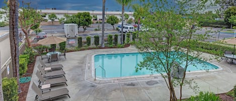 A pool area with lounge chairs, a pool, and surrounding greenery.