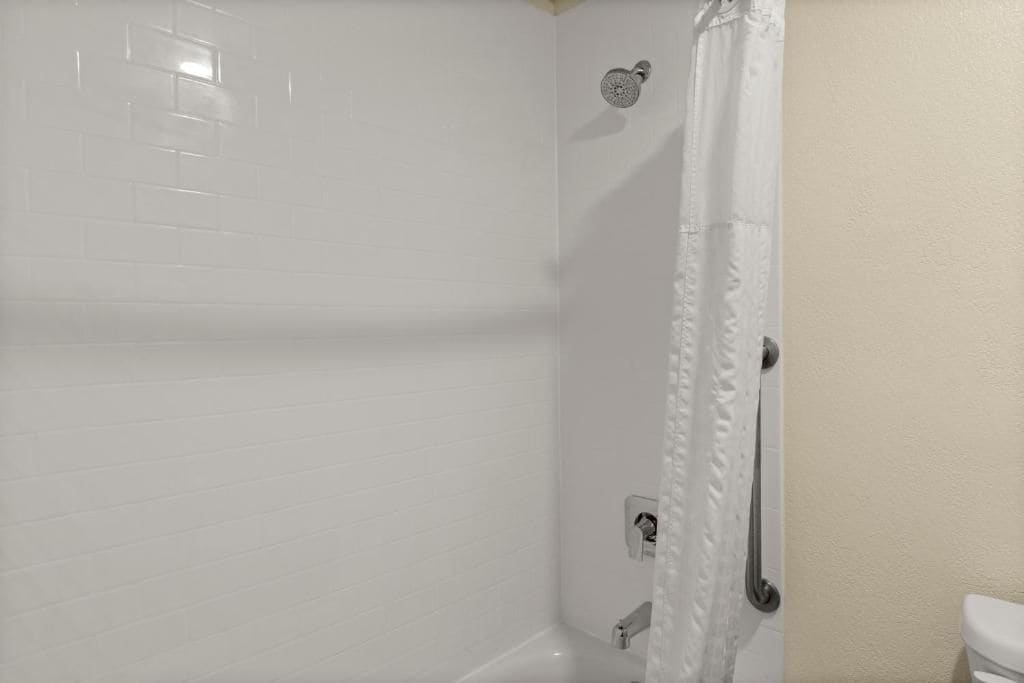 A bathroom with white tiled walls, a shower with a curtain, a toilet, and a handrail.