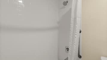 A bathroom with white tiled walls, a shower with a curtain, a toilet, and a handrail.