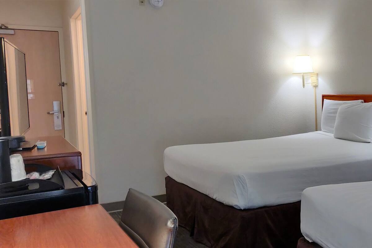 A hotel room with two beds, a desk, a chair, a mirror, and two bedside lamps.