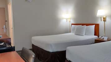 Une chambre d’hôtel avec deux lits, un bureau, une chaise, un miroir et deux lampes de chevet.