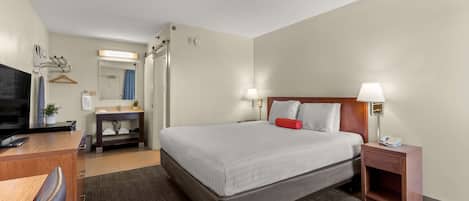 A hotel room with a bed, bedside tables, a desk, a chair, a TV, a mirror, and a bathroom door.