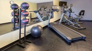 Un gimnasio con cintas de correr, elípticas y un estante de pelotas de ejercicios.