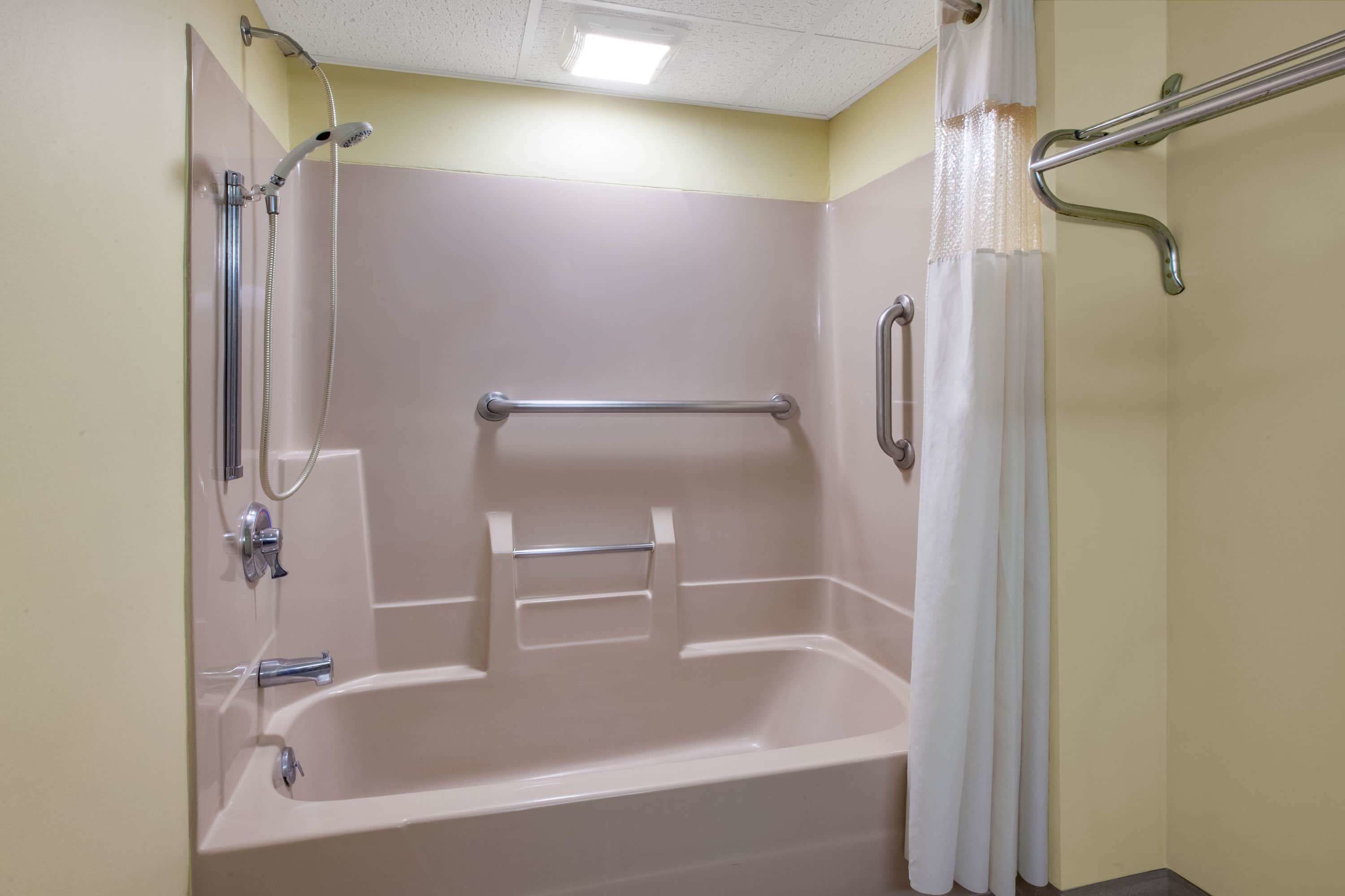 A bathroom with a bathtub, a shower, and a handrail.