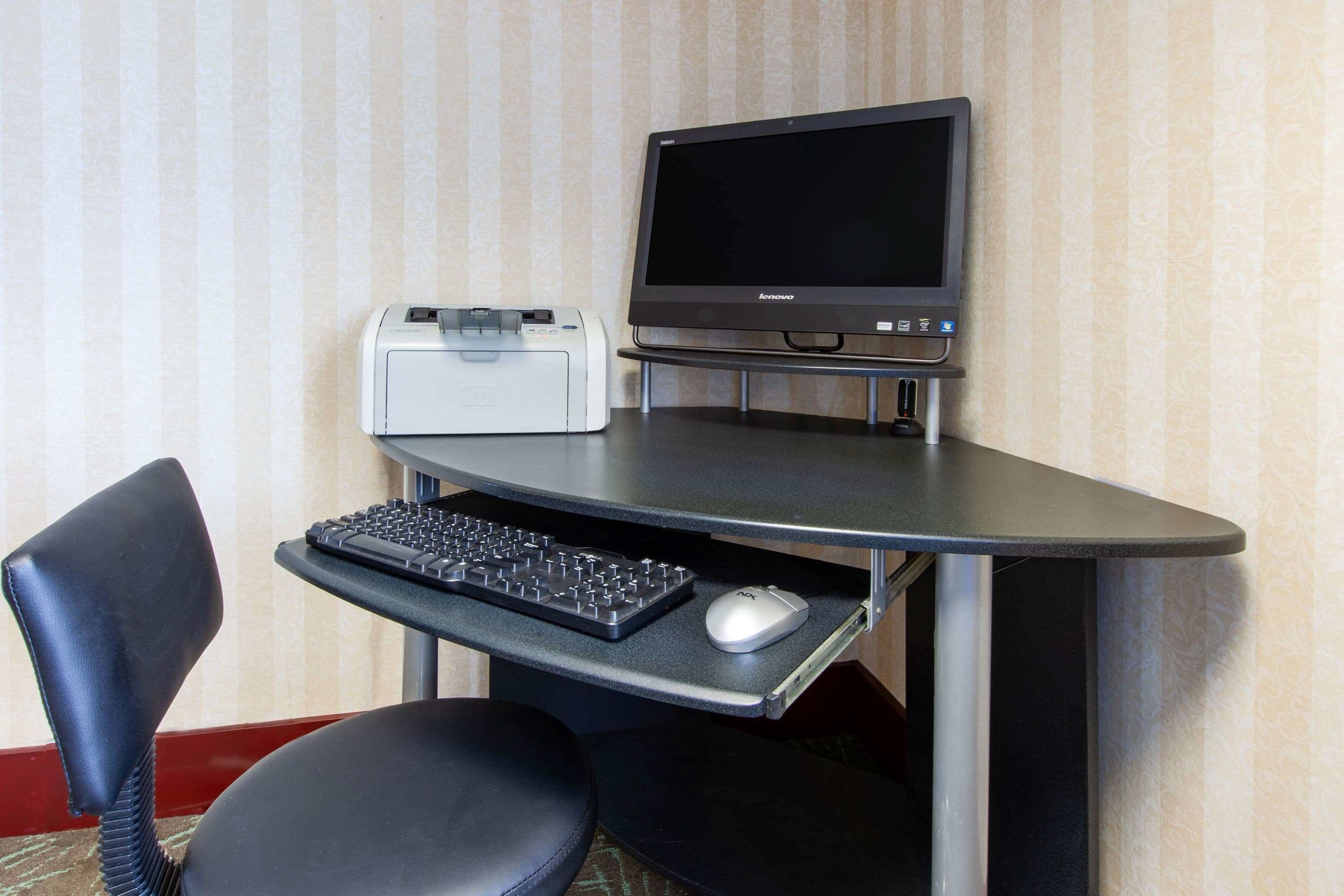 A corner desk setup with a monitor, keyboard, mouse, and printer.
