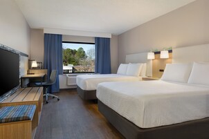 Habitación de hotel con dos camas, un escritorio, una silla, un televisor y una ventana con cortinas.