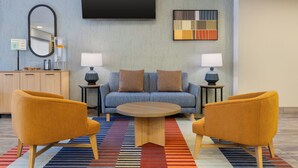Una sala de estar moderna con un sofá, dos sillones, una mesa de centro, un televisor de pantalla plana, un espejo y una alfombra estampada.