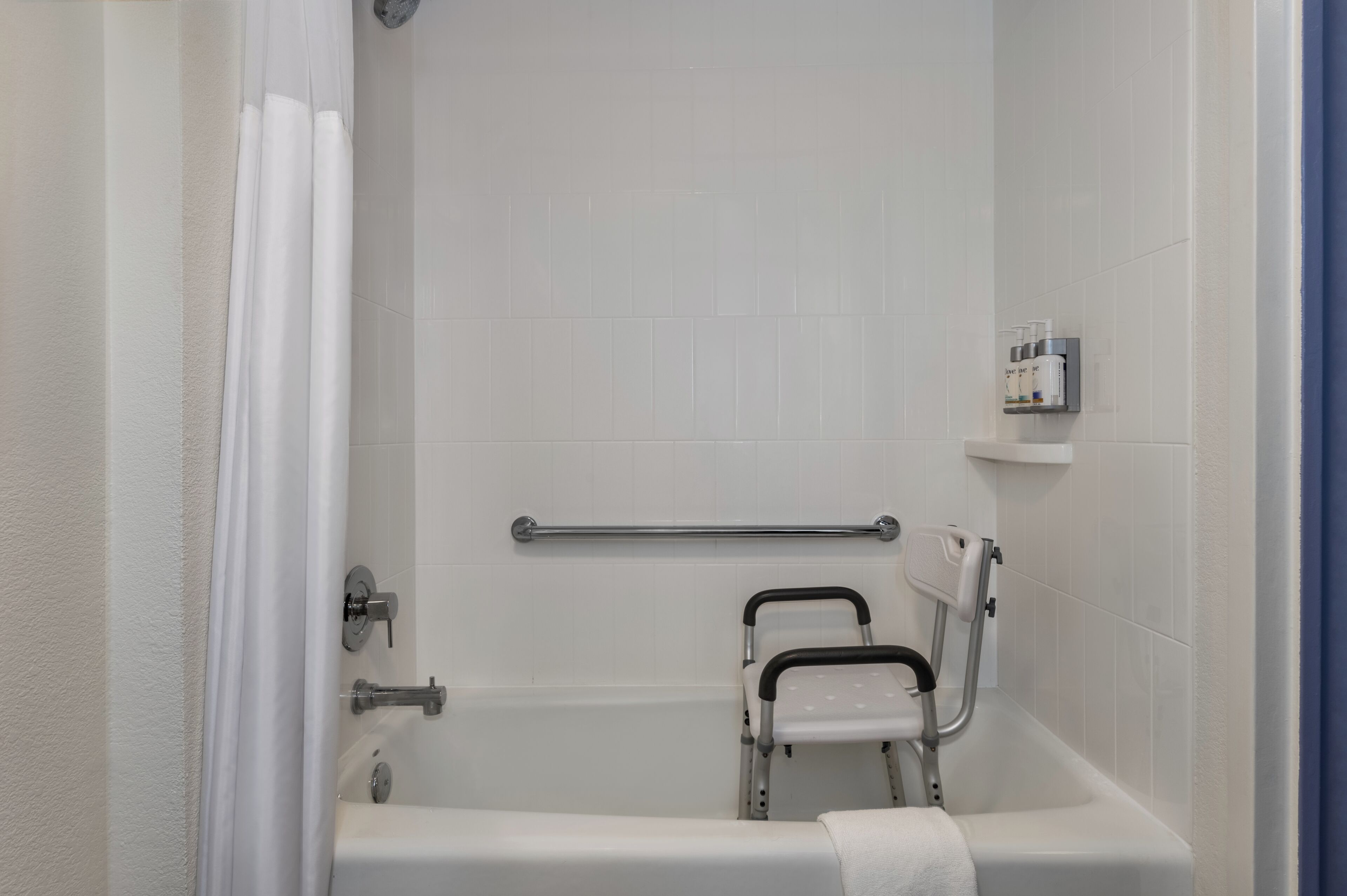 Un baño con una bañera blanca, una barra de apoyo, una cortina de ducha y un estante con artículos de aseo.