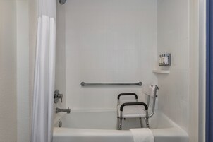 Un baño con una bañera blanca, una barra de apoyo, una cortina de ducha y un estante con artículos de aseo.