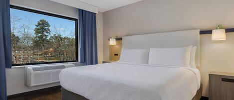 Une chambre d’hôtel avec un grand lit, une fenêtre avec des rideaux, un radiateur fixé au mur et une table de chevet.
