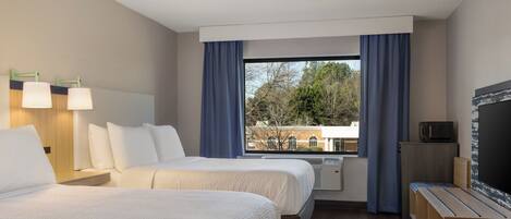 Quarto de hotel com duas camas, televisão, escrivaninha e janela com cortinas.