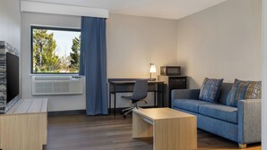 Una habitación de hotel moderna con escritorio, silla, sofá, televisor y un ventanal con cortinas.