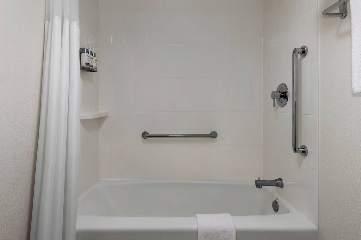 A white bathtub with a grab bar, a towel rack, and a shower curtain.