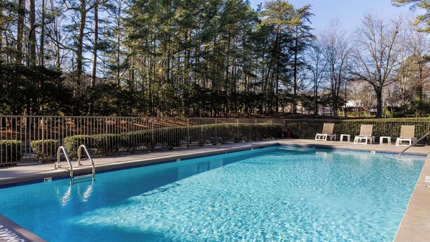 Piscina rectangular con una escalera metálica, rodeada por una cerca metálica y árboles.