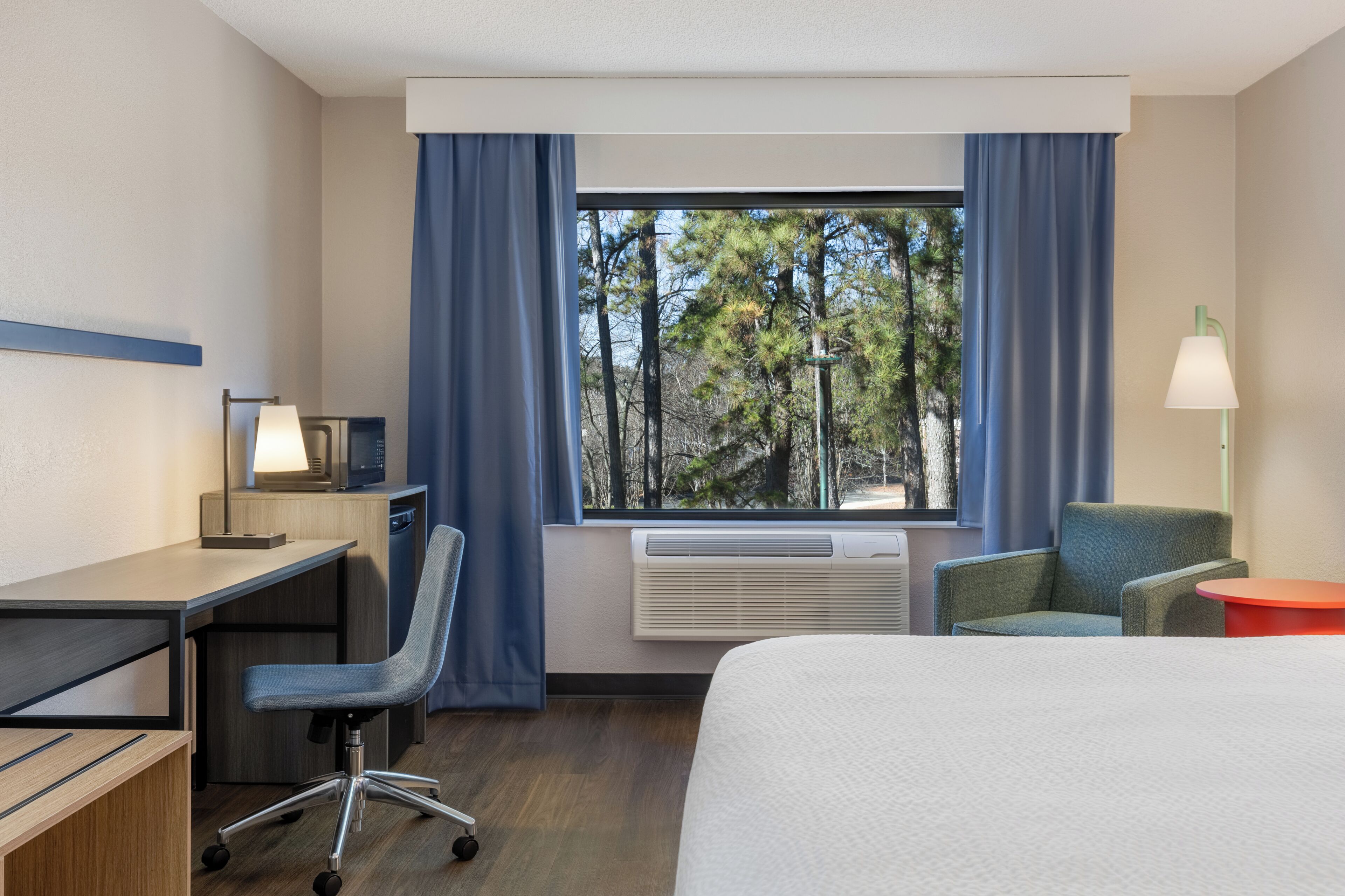 A hotel room with a bed, desk, chair, and a window with curtains.