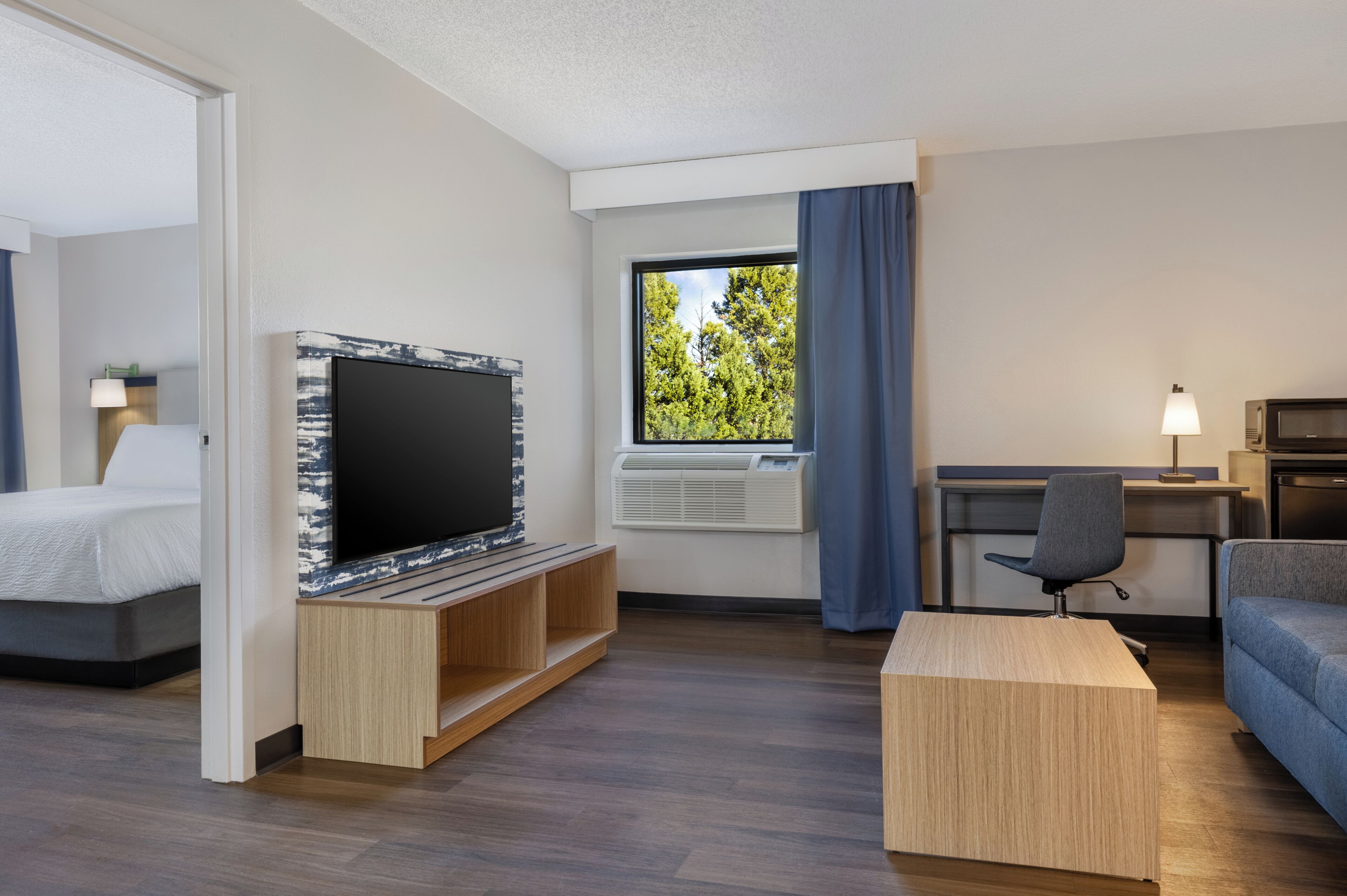 Habitación de hotel con cama, televisión, escritorio, silla y ventana con cortinas.
